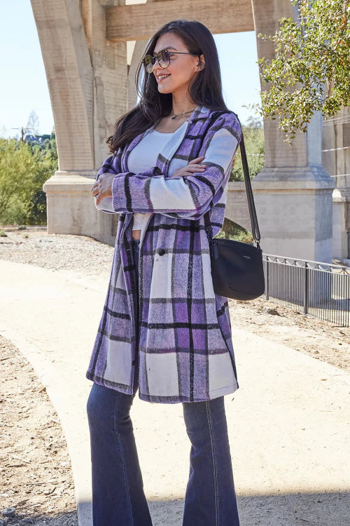 Woman wearing a purple plaid coat with a black handbag outdoors.