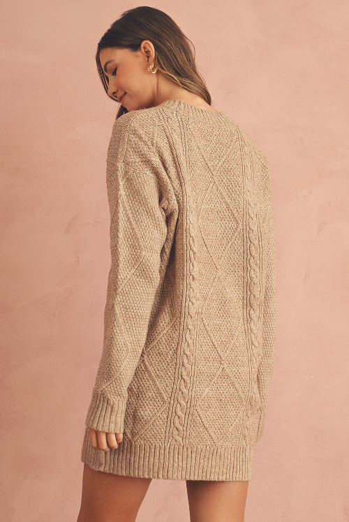 Woman wearing a beige cable knit sweater dress against a pink background