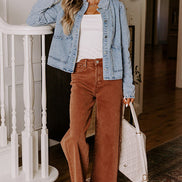 Woman in a denim jacket and brown pants standing in a home setting.