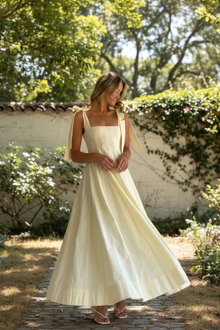 Woman wearing a light yellow dress with ribbon straps against a white background