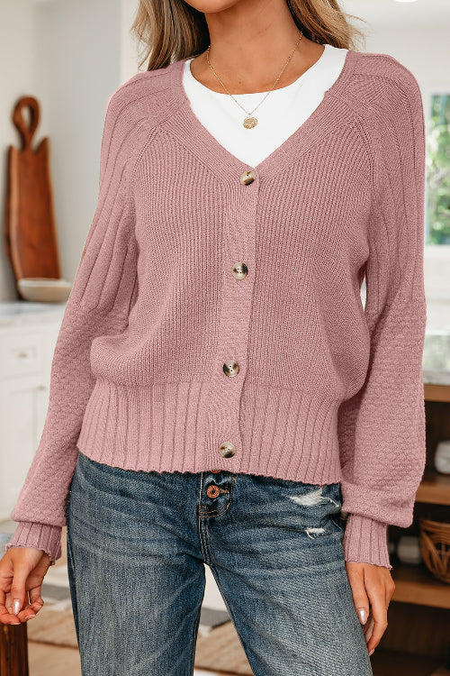 Person wearing a pink cardigan over a white shirt with blue jeans indoors.