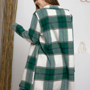 Woman wearing a green and white plaid coat in a room with a mirror and plant.