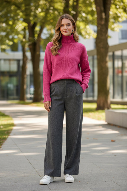 A person wearing a bright pink ribbed turtleneck sweater with a diamond-patterned knit design on the chest, 