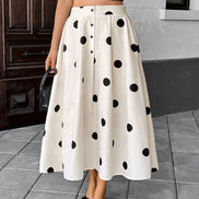 A woman wearing a high-waisted, knee-length A-line midi skirt in cream with black polka dots, styled with a black crop top