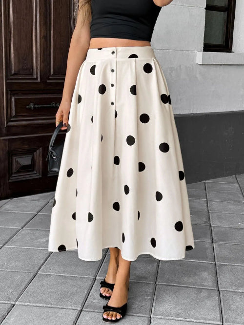 A woman wearing a high-waisted, knee-length A-line midi skirt in cream with black polka dots, styled with a black crop top