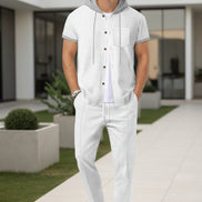A man wearing a white short-sleeve button-front hooded shirt with gray trim and matching white pants, 