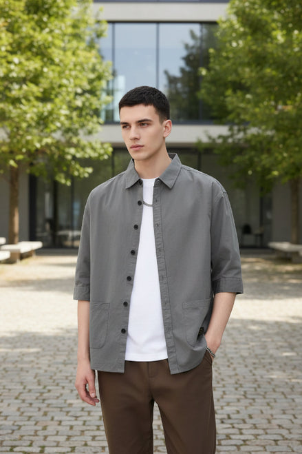 Person wearing a gray button-up shirt over a white shirt with a plain background