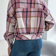 Person wearing a plaid shirt and blue jeans against a white wall.