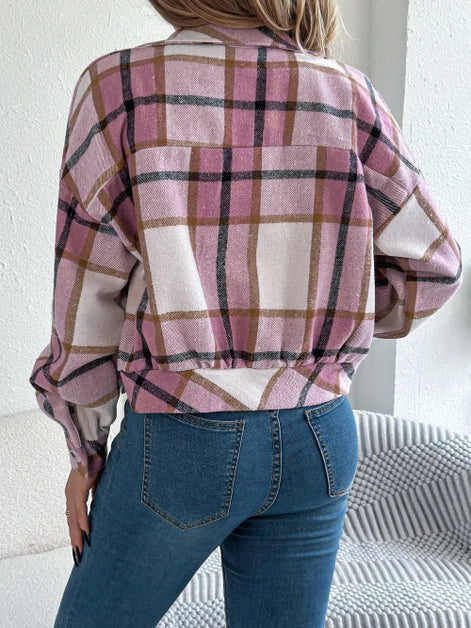 Person wearing a plaid shirt and blue jeans against a white wall.