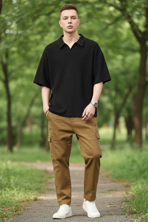 Person wearing a black polo shirt and brown pants on a white background