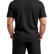 A man viewed from the back wearing a black short-sleeve polo shirt and matching black shorts, 