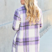 Person wearing a purple and white plaid coat standing against a light-colored wall.