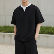 Person wearing a black outfit with a white collar on a plain background