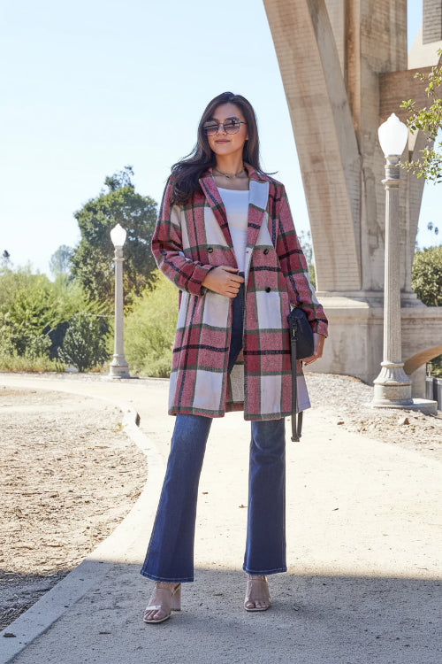 Woman wearing a plaid coat and blue jeans standing outdoors 