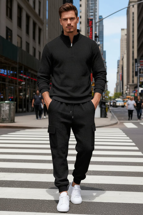 A man wearing a matching black textured quarter-zip pullover and jogger 