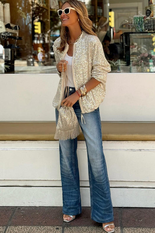Woman wearing a beige cardigan and blue jeans standing on steps in an urban setting.