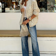 Woman wearing a beige cardigan and blue jeans standing on steps in an urban setting.