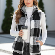 Person wearing a black and white checkered vest holding a coffee cup indoors.