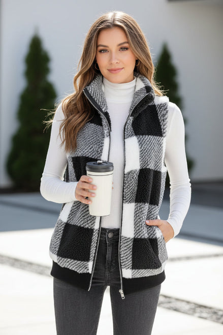 Person wearing a black and white checkered vest holding a coffee cup indoors.