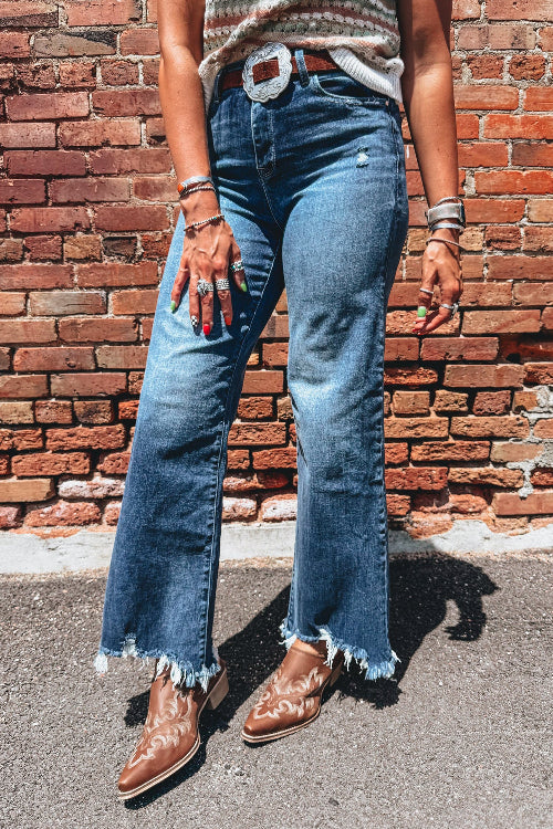 Person wearing blue jeans and brown shoes standing against a brick wall.