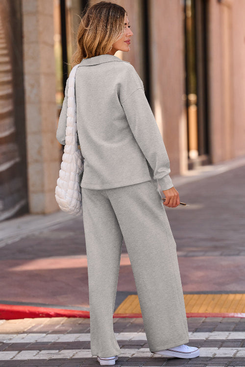 A woman wearing a light gray two-piece lounge set consisting of a long-sleeve top and matching wide-leg pants, standing on a city sidewalk.