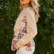 Woman wearing a plaid shirt over a beige long-sleeve shirt with white pants against a green leafy background