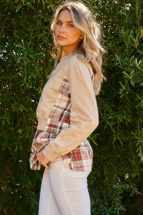 Woman wearing a plaid shirt over a beige long-sleeve shirt with white pants against a green leafy background