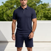 A man wearing a dark navy blue short-sleeve polo shirt and matching textured shorts, 