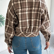 Person wearing a brown plaid shirt and blue jeans in a minimal indoor setting