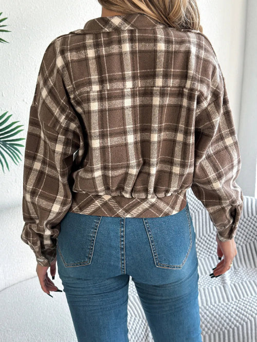 Person wearing a brown plaid shirt and blue jeans in a minimal indoor setting