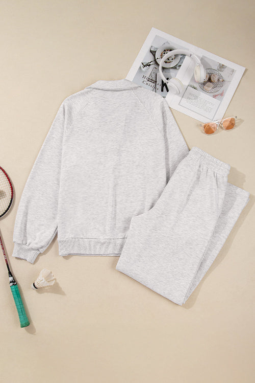 Gray sweatshirt and pants set with a tennis racket and newspaper on a beige background