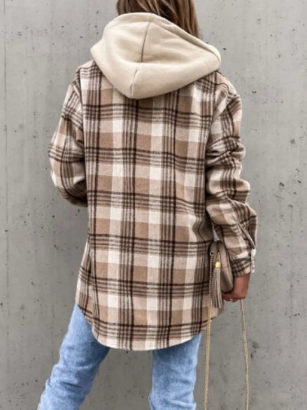 Person wearing a plaid shirt with a beige hoodie against a gray concrete wall