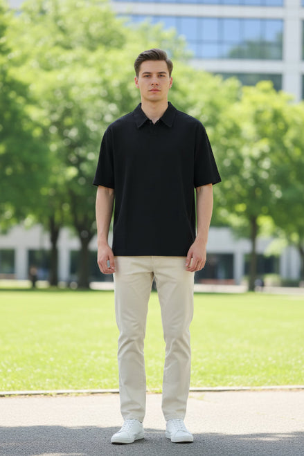 Person wearing a black polo shirt and pants against a gray concrete wall.