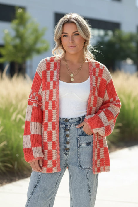 Person wearing a red and beige checkered cardigan over a white top and blue jeans on a white background