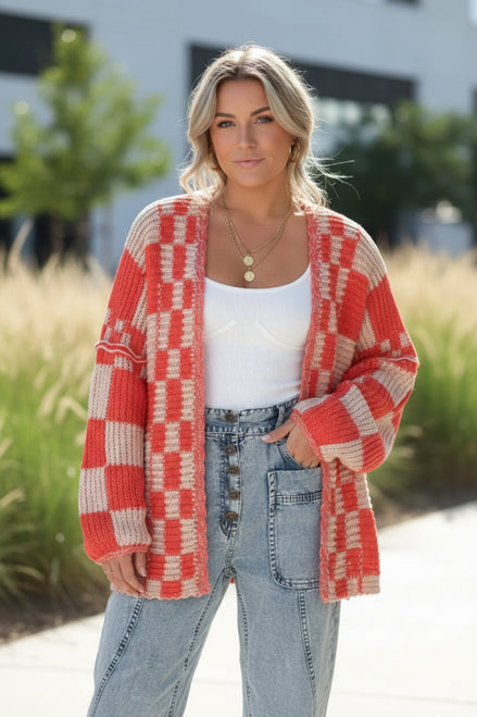 Person wearing a red and beige checkered cardigan over a white top and blue jeans on a white background
