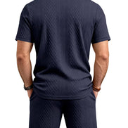 A man viewed from the back wearing a dark navy blue short-sleeve polo shirt and matching shorts, 