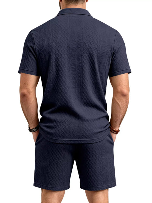 A man viewed from the back wearing a dark navy blue short-sleeve polo shirt and matching shorts, 