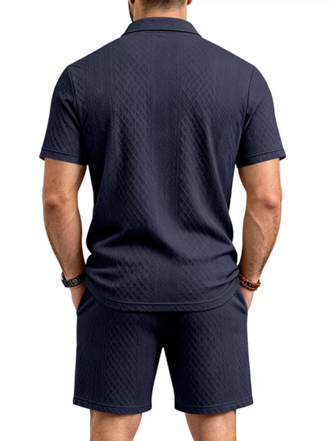 A man viewed from the back wearing a dark navy blue short-sleeve polo shirt and matching shorts, 