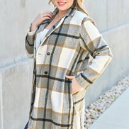 Woman wearing a plaid coat standing against a light-colored wall.