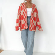 Person wearing a red and beige checkered cardigan over a white top and blue jeans on a plain background