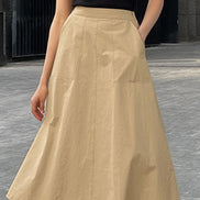 Person wearing a beige skirt and black top on a gray pavement background