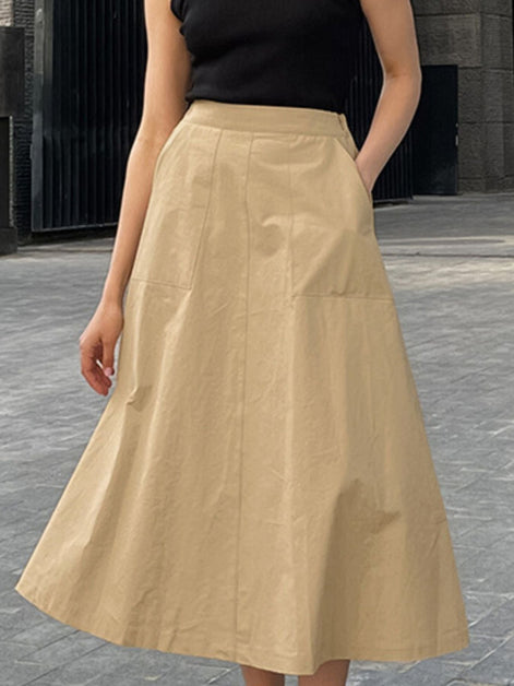 Person wearing a beige skirt and black top on a gray pavement background