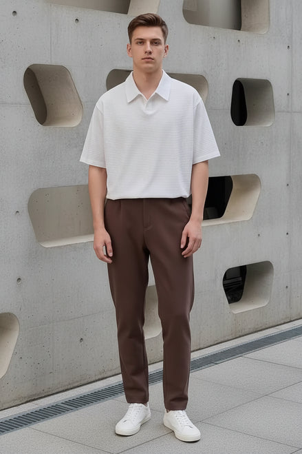 Person wearing a white textured shirt and brown pants, holding a black bag.