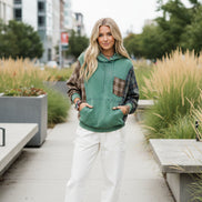 A woman wearing a green hooded sweatshirt with brown plaid sleeves and a matching plaid chest pocket, 