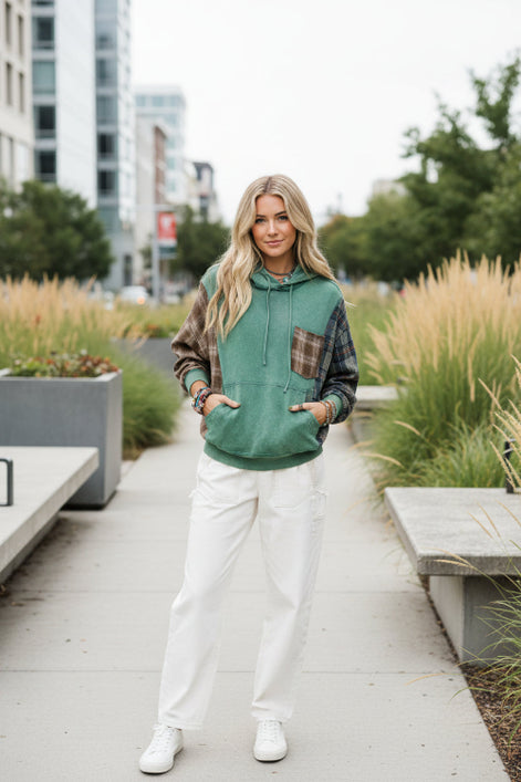 A woman wearing a green hooded sweatshirt with brown plaid sleeves and a matching plaid chest pocket, 
