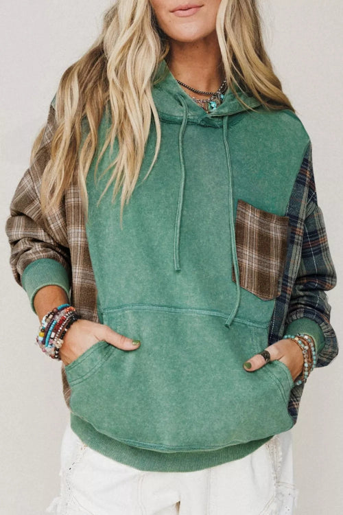 A woman wearing a green hooded sweatshirt with brown plaid sleeves and a matching plaid chest pocket, 