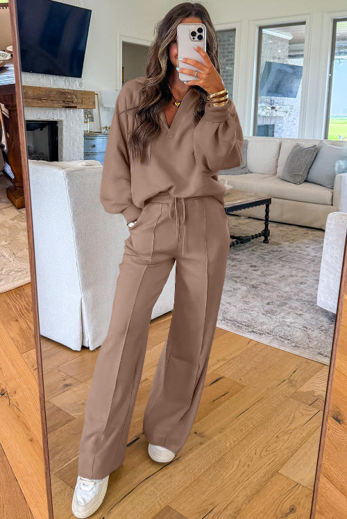 Woman taking a mirror selfie wearing a brown outfit in a living room.