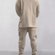 A person shown from the back wearing a matching beige cable-knit sweater and jogger pants set, 