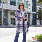 Woman wearing a purple plaid coat and blue pants standing outdoors.