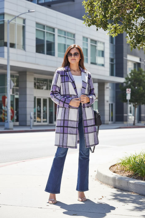 Woman wearing a purple plaid coat and blue pants standing outdoors.